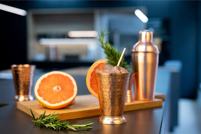 Ein erfrischender Cocktail mit Orangensaft, serviert in einem stilvollen Kupferbecher mit Eiswürfeln und einer Orangenscheibe als Garnitur – perfekt für einen geselligen Sommerabend.